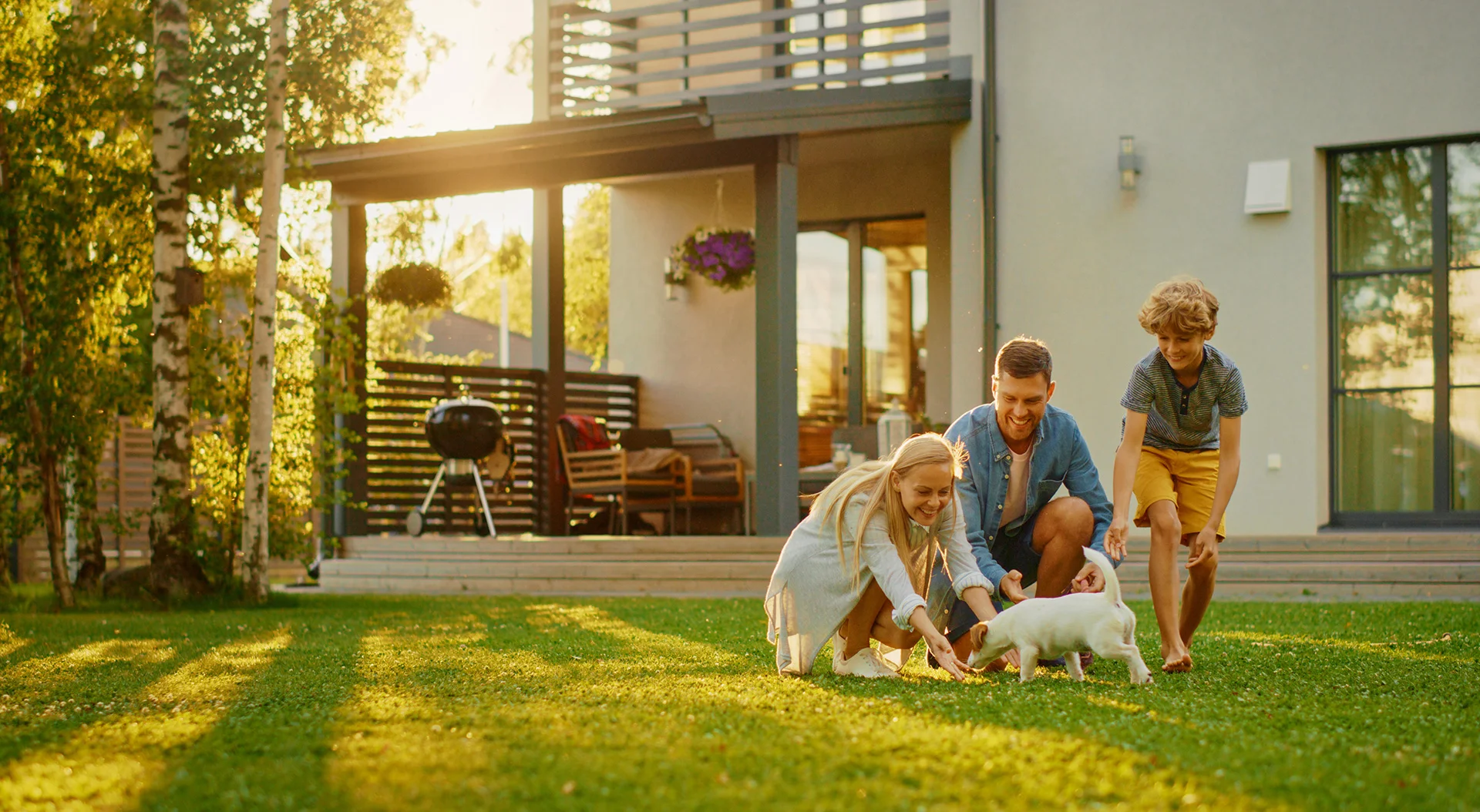 Smiling Father, Mother and Son Pet and Play with Smooth Fox Terrier Retriever Dog. Sun Shines on Idyllic Happy Family with Loyal Pedigree Dog have Fun at the Idyllic Suburban House Backyard